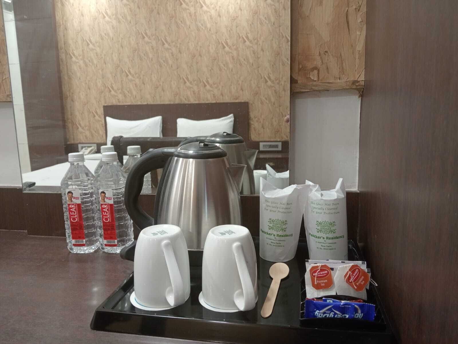 Tavolo da colazione in camera d'albergo con bollitore, due tazze bianche, due bottiglie d'acqua, due bustine di tè, un cucchiaino di legno e una scatola di tè.