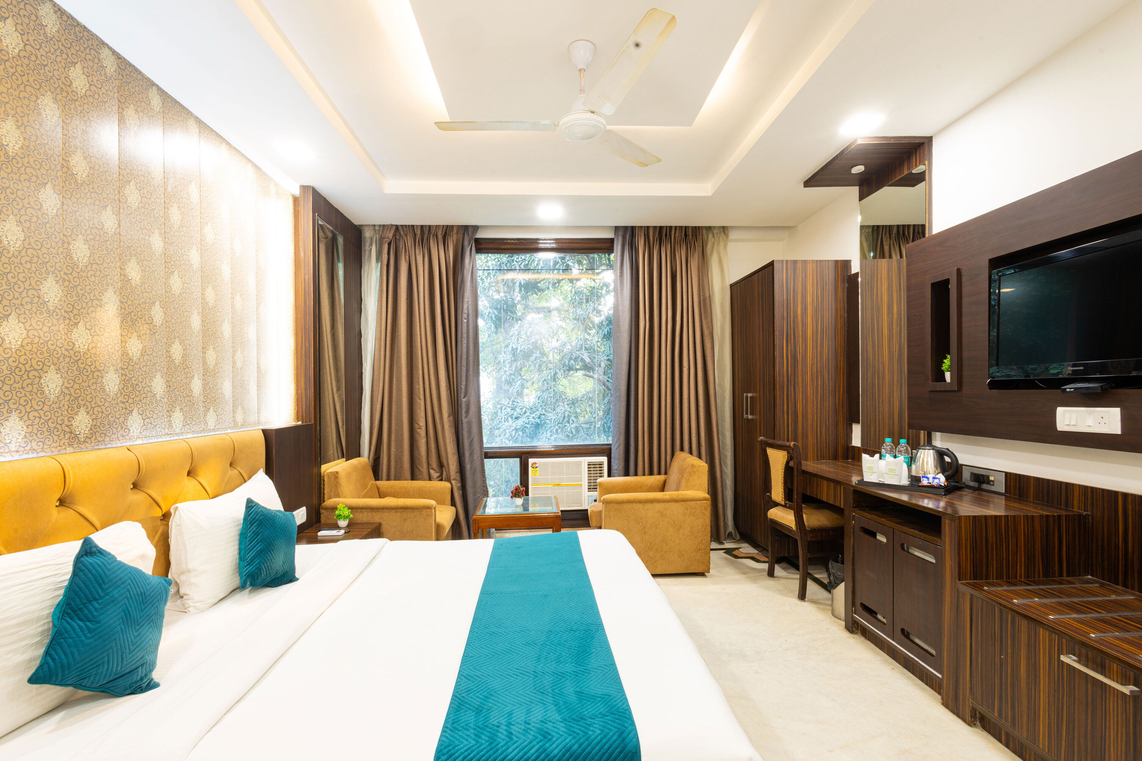 A hotel room with a large bed, a TV, a desk, and a view of the outdoors.