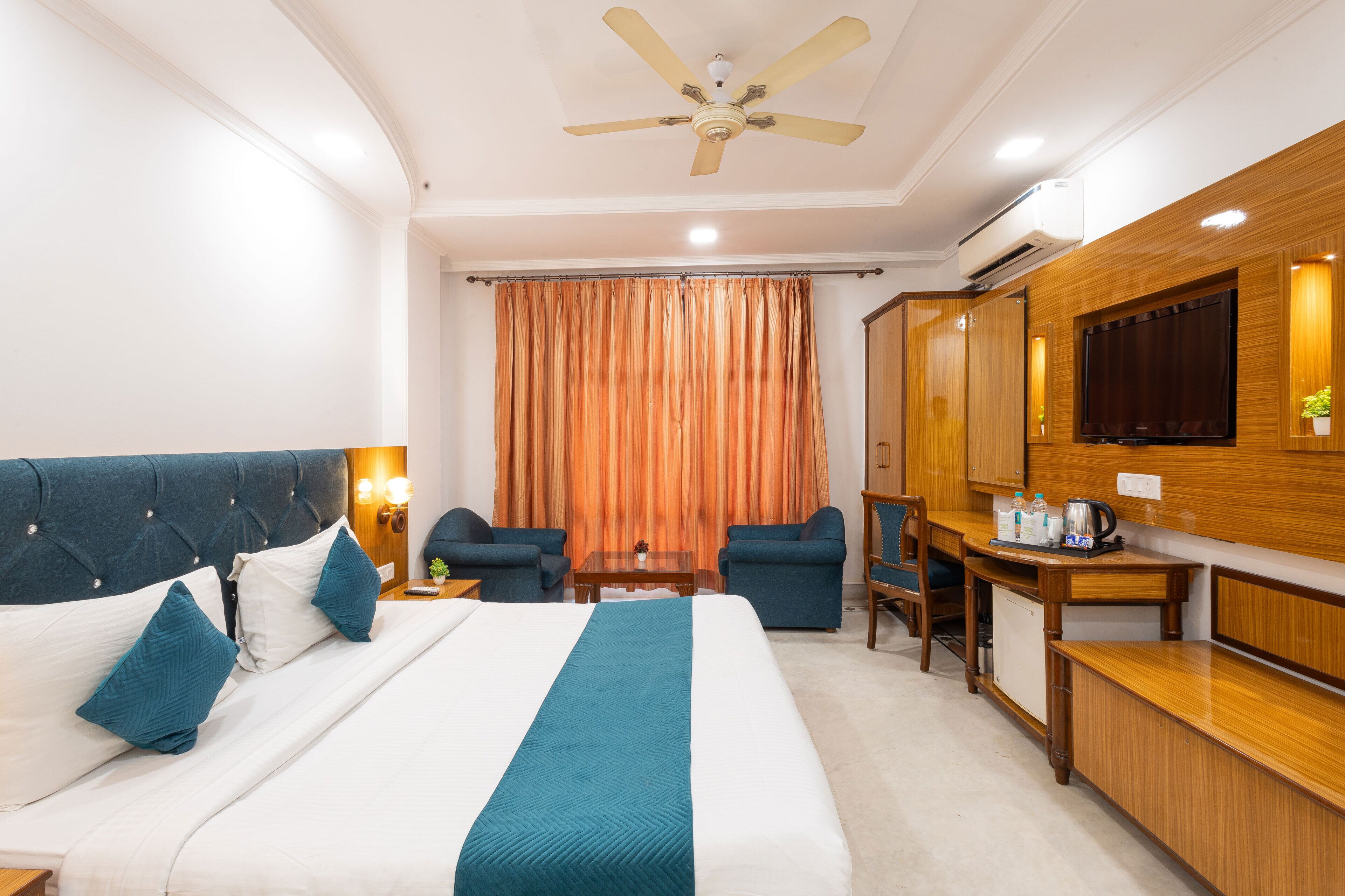 A hotel room with a large bed, two armchairs, a desk with a television, and a ceiling fan.