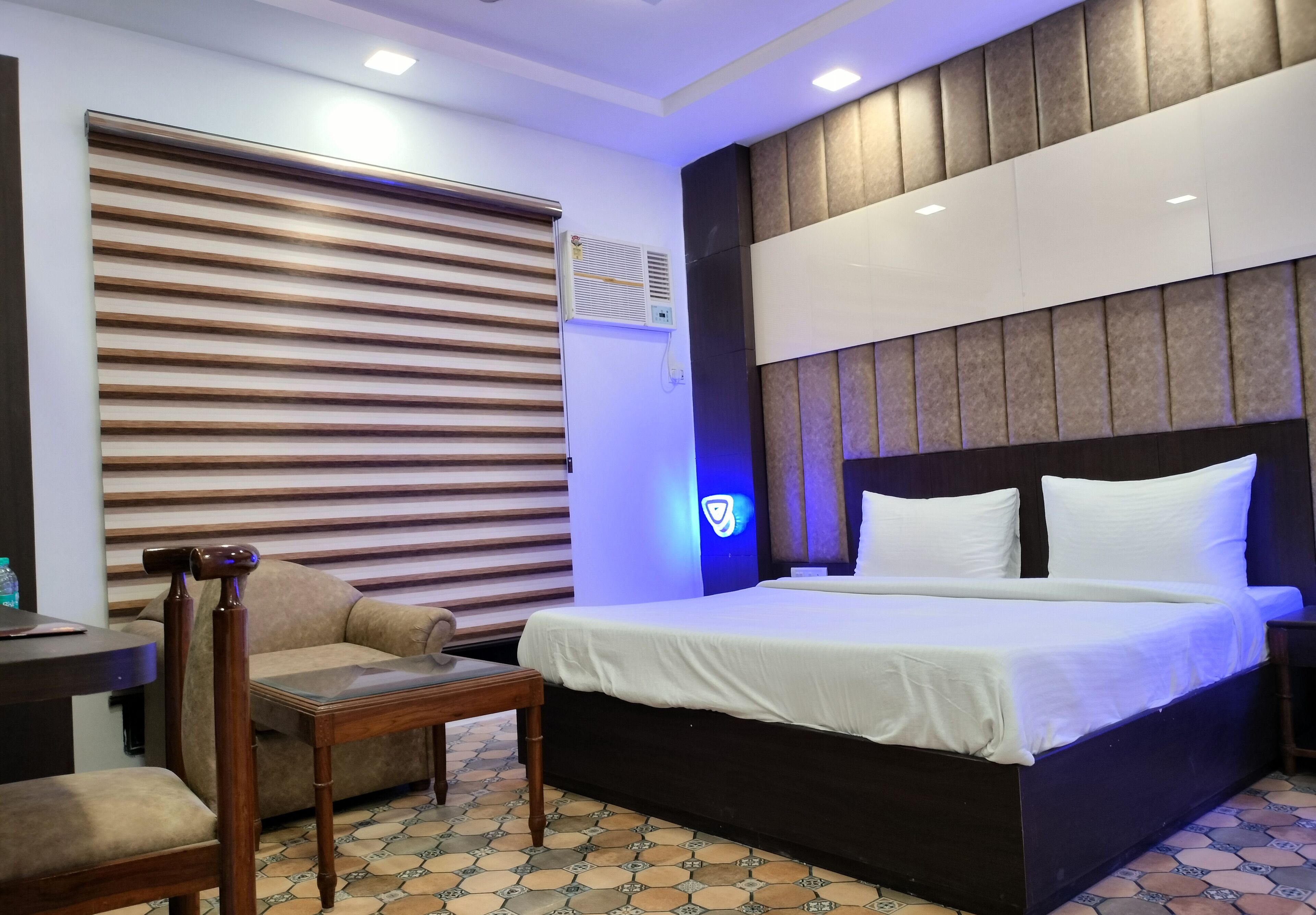 A hotel room with a bed, a sofa, a wooden chair, a table, and a patterned floor.