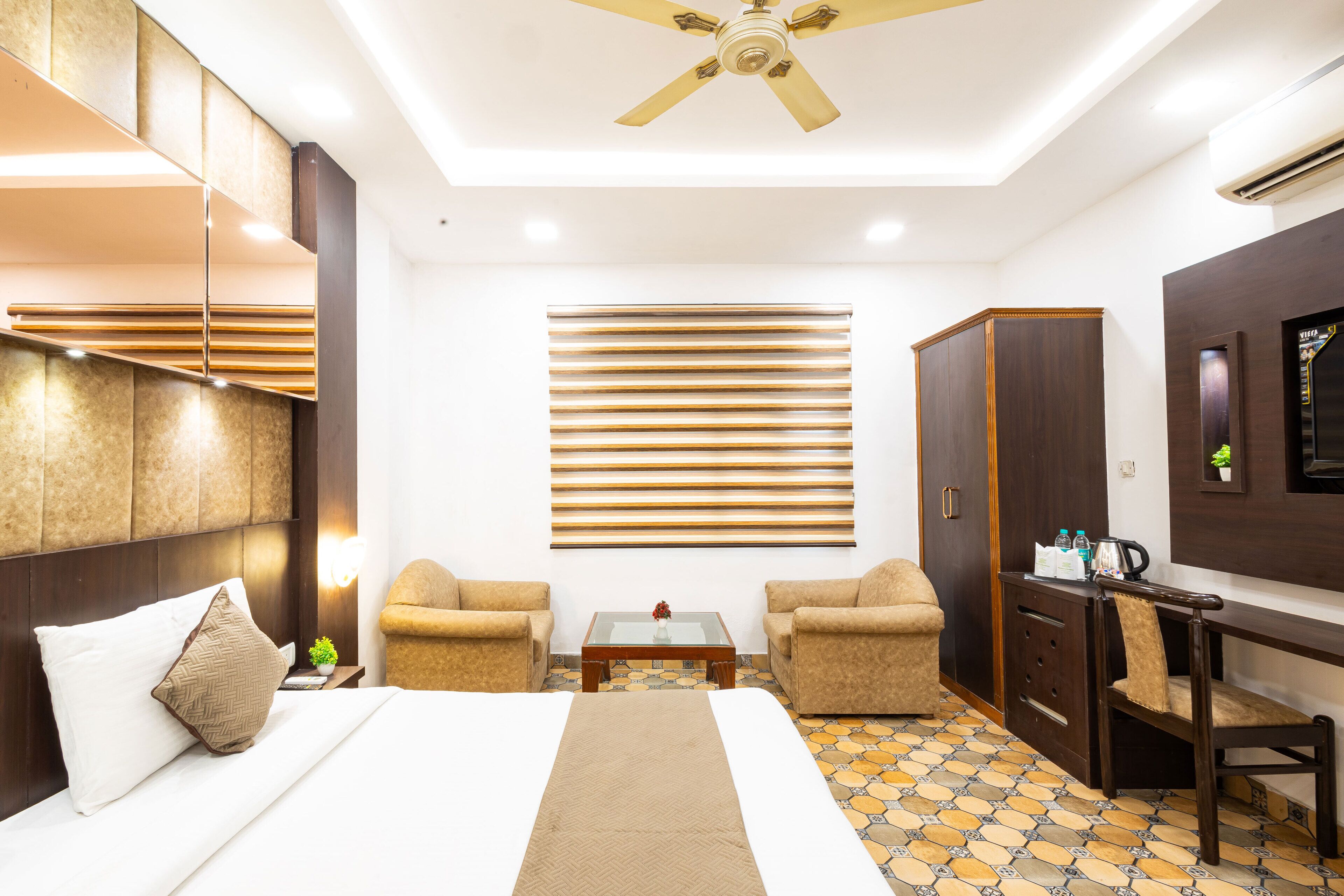 A hotel room with a bed, two armchairs, a small table, a desk, and a wardrobe.