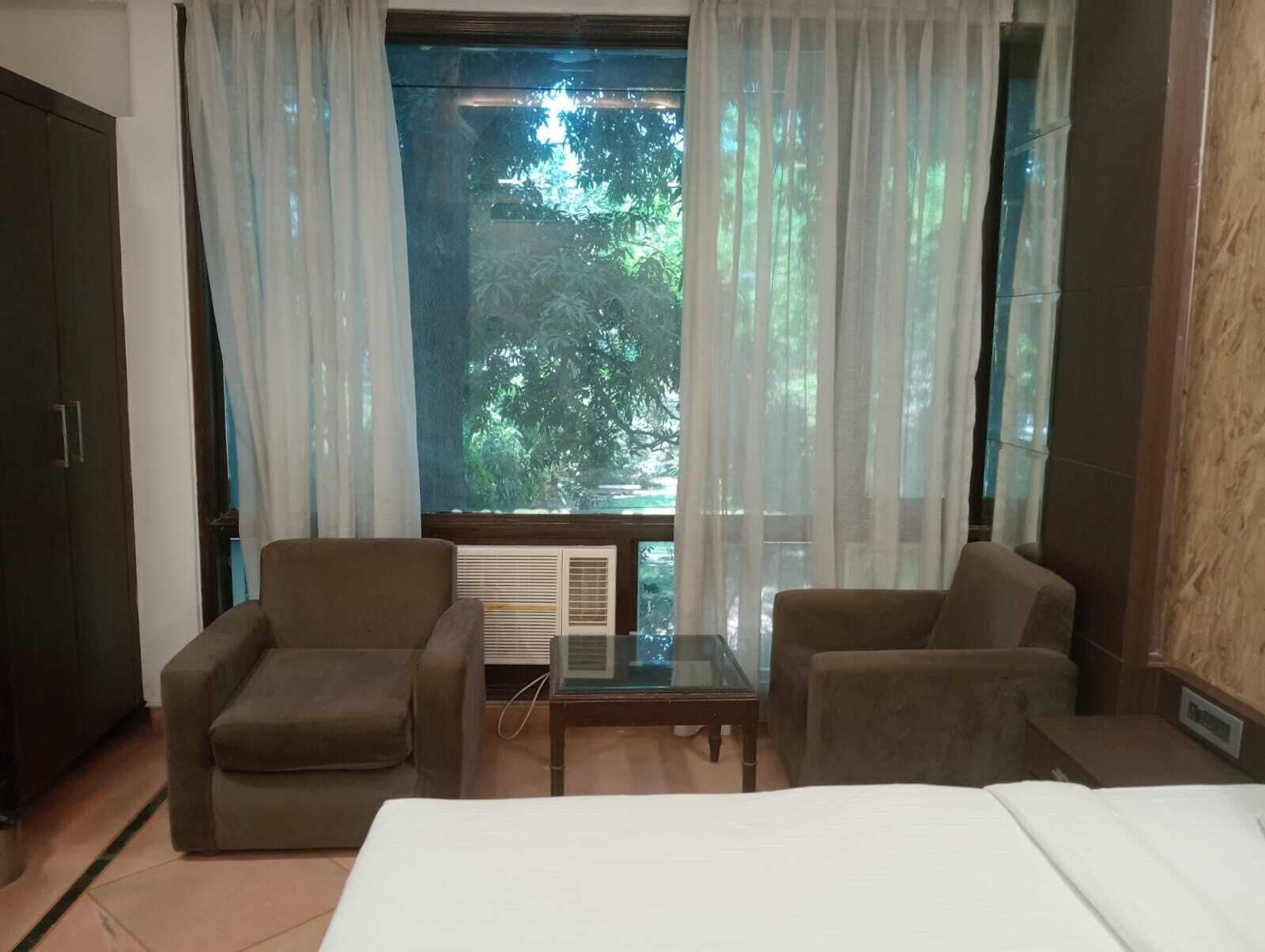 A hotel room with a bed, two armchairs, a small table, and a window with curtains.