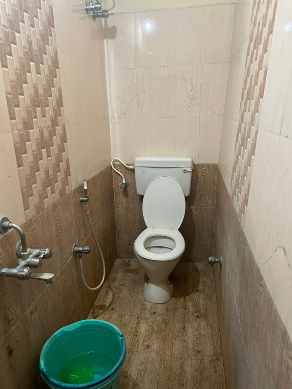 Une petite salle de bain avec des toilettes, une douche et un seau.