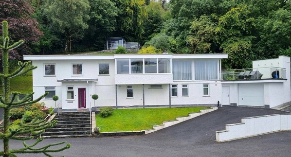 A modern two-story house with a red door, a small front garden, and a driveway leading to a garage. - Detached 4 Bed Home, Hot Tub & Lake View - Pets OK (Bowness-on-Windermere)
