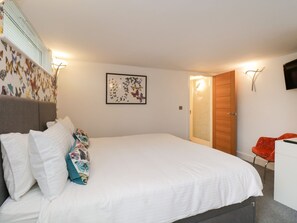 A bedroom with a bed, pillows, a wall-mounted TV, a door, and a window with blinds. - Detached 4 Bed Home, Hot Tub & Lake View - Pets OK (Bowness-on-Windermere)