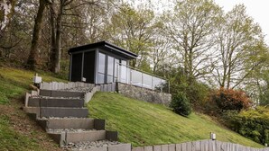 Ein modernes Gebäude mit Glasfassade, umgeben von einer Steinsichtmauer und Treppen, die davorführen.