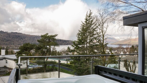 Ein Whirlpool auf einem Balkon mit Blick auf einen See, Bäume und eine Berglandschaft.