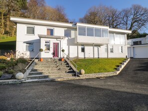 A modern two-story building with a red door, a staircase leading to the entrance, and a well-maintained lawn. - Detached 4 Bed Home, Hot Tub & Lake View - Pets OK (Bowness-on-Windermere)