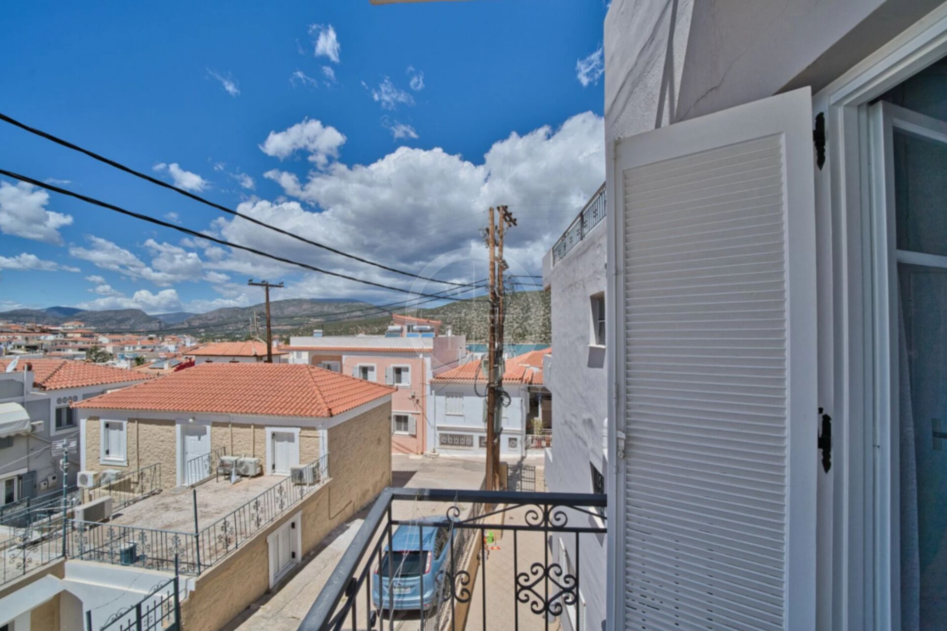 A balcony with a view of a residential area, including houses with red-tiled roofs and a distant mountain range.