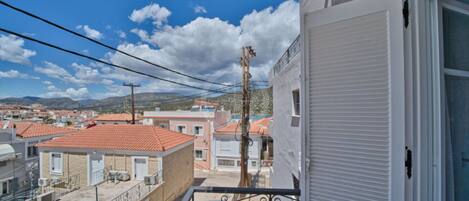 A balcony with a view of a residential area, including houses with red-tiled roofs and a distant mountain range.