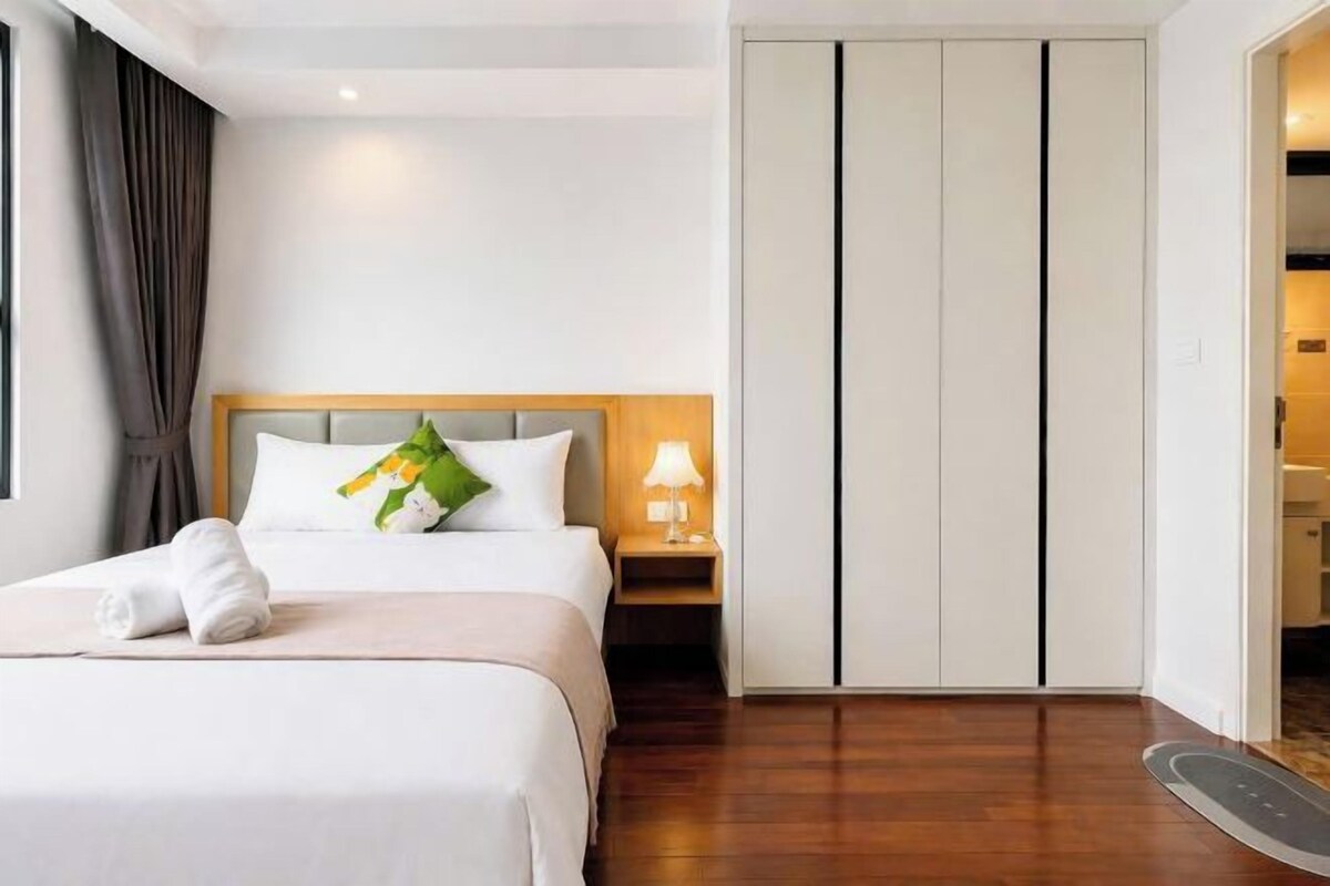 A hotel room with a bed, a nightstand, a lamp, a wardrobe, and a door leading to another room.