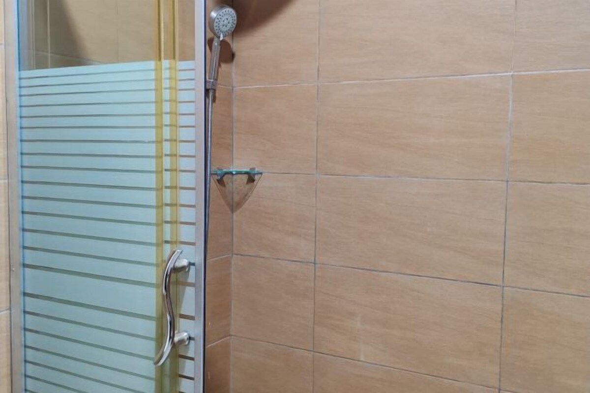 Ein Badezimmer mit beigen Fliesen, einer Duschkabine aus Glas und einem Metall-Duschkopf.