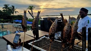 Una griglia con diversi spiedini di pesce, una ciotola di limoni e una persona vestita da chef.