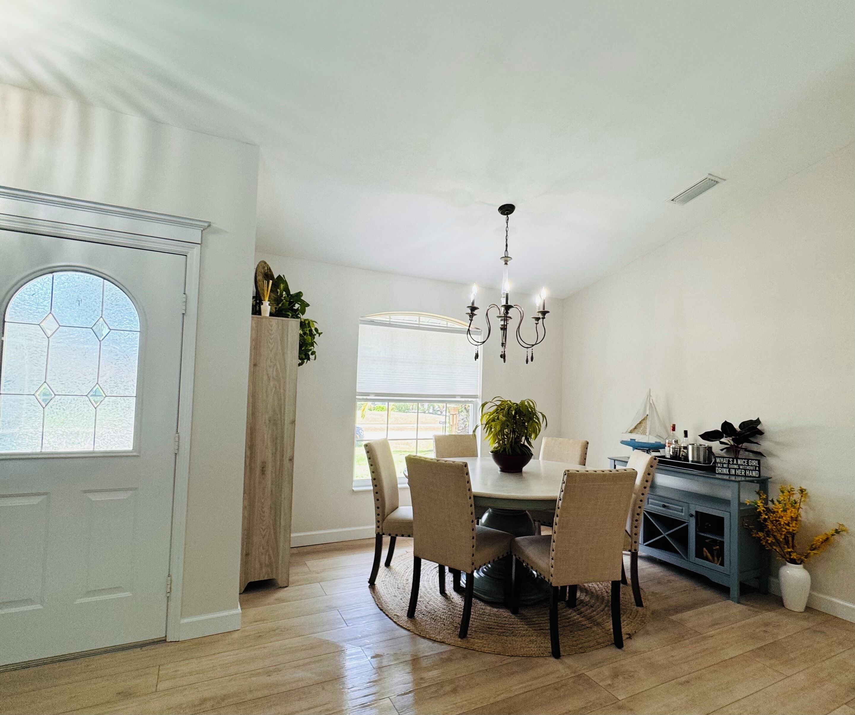 A dining area with a round table, four chairs, a chandelier, and a potted plant.
