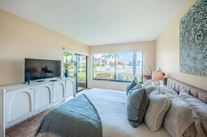 Un dormitorio con cama, televisor, ventana con vistas y un cuadro en la pared.