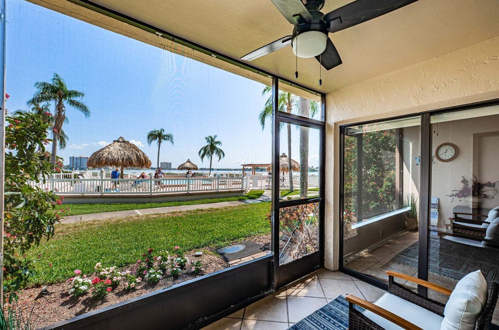 A balcony with a view of a beach, a thatched-roof structure, and a palm tree.