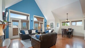 A spacious living room with a high ceiling, a fireplace, and a dining area with a table and chairs. - Magnificent Mountain Penthouse - Pool & Hot Tub (Canmore)