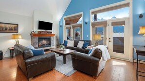 A living room with a fireplace, leather sofas, a coffee table, and a television. - Magnificent Mountain Penthouse - Pool & Hot Tub (Canmore)