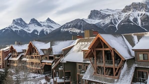 A row of wooden cabins with snow-covered roofs, set against a backdrop of snow-capped mountains. - Magnificent Mountain Penthouse - Pool & Hot Tub (Canmore)