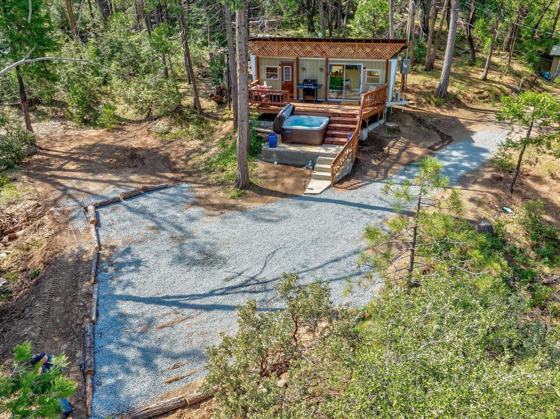 Une cabane dotée d’un bain à remous, d’une terrasse et d’un patio en gravier, le tout entouré d’arbres.