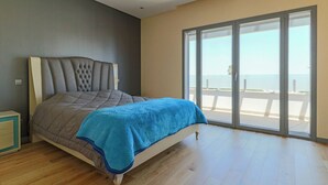 Un dormitorio con una cama grande, una puerta corrediza de vidrio a un balcón y piso de madera.