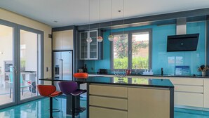 Una cocina moderna con una isla grande, taburetes de bar coloridos y vistas a la vegetación exterior.