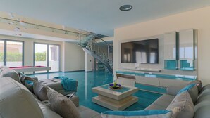 Amplia sala de estar con piscina, escalera y televisor instalado en la pared.