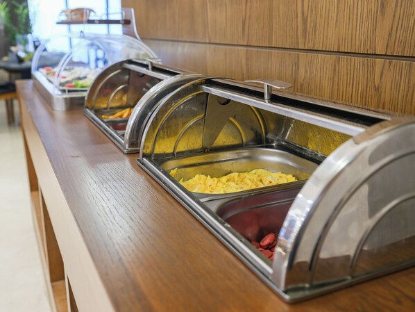 Una barra de buffet con diversos alimentos en recipientes cubiertos.