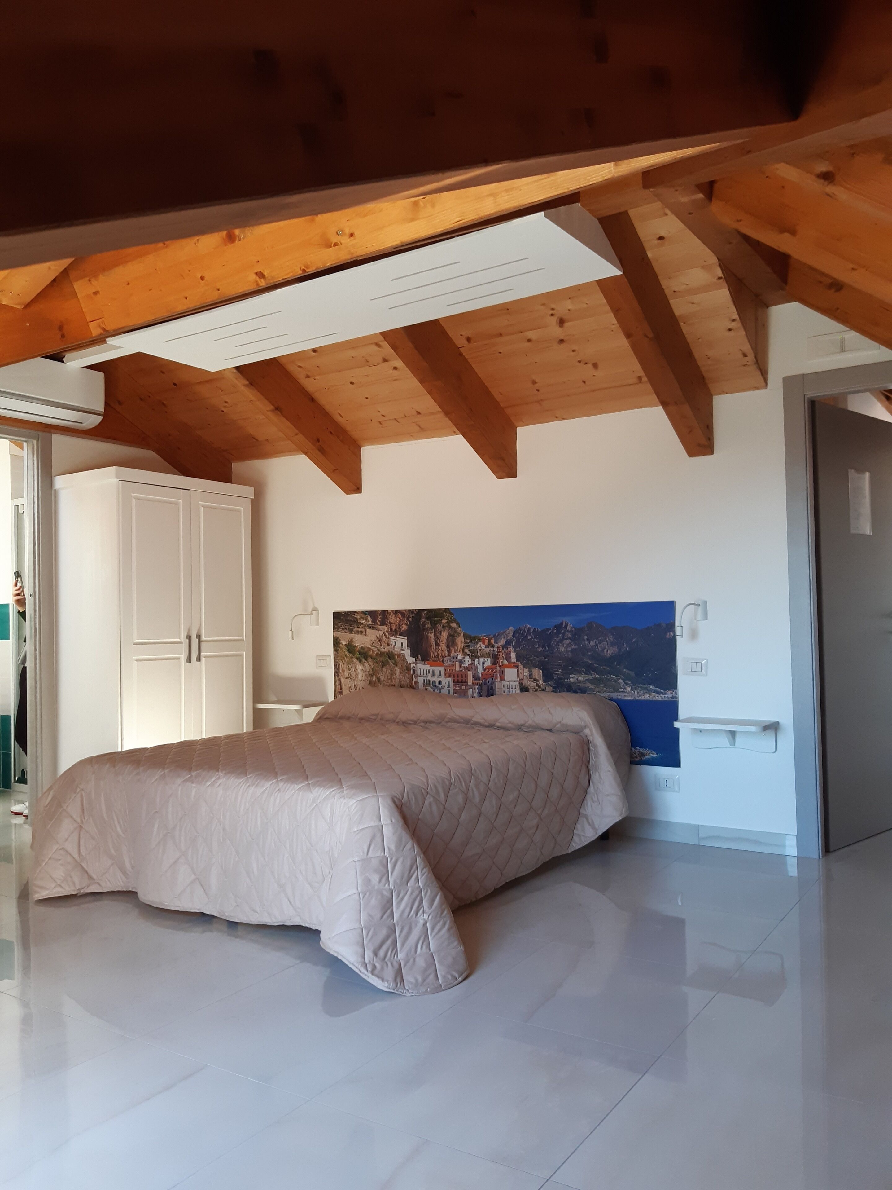 Un dormitorio con una cama grande, vigas de madera en el techo, un armario blanco y una estantería de pared.