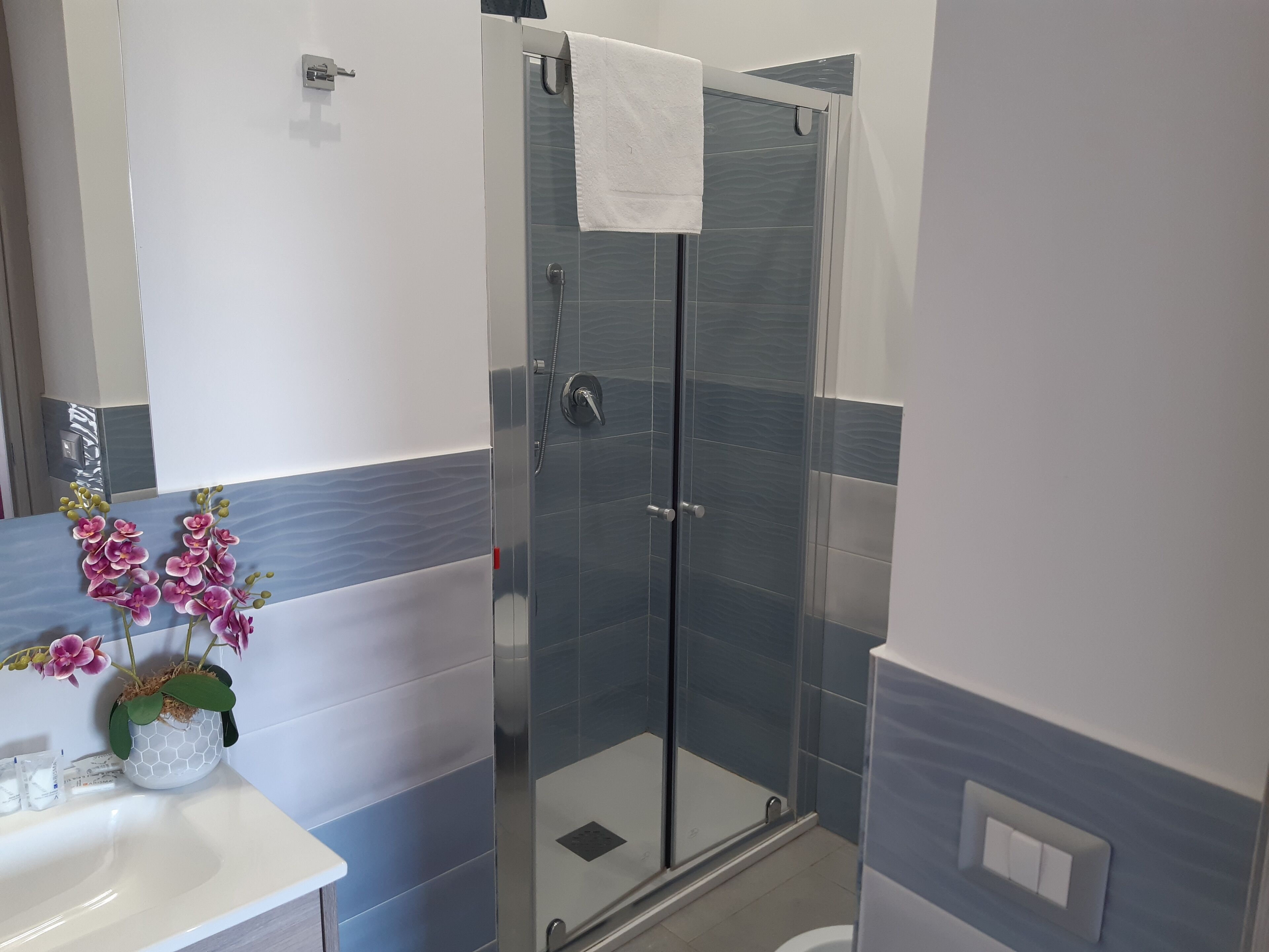 A modern bathroom with a glass shower enclosure, a white sink, and a vase with pink orchids.