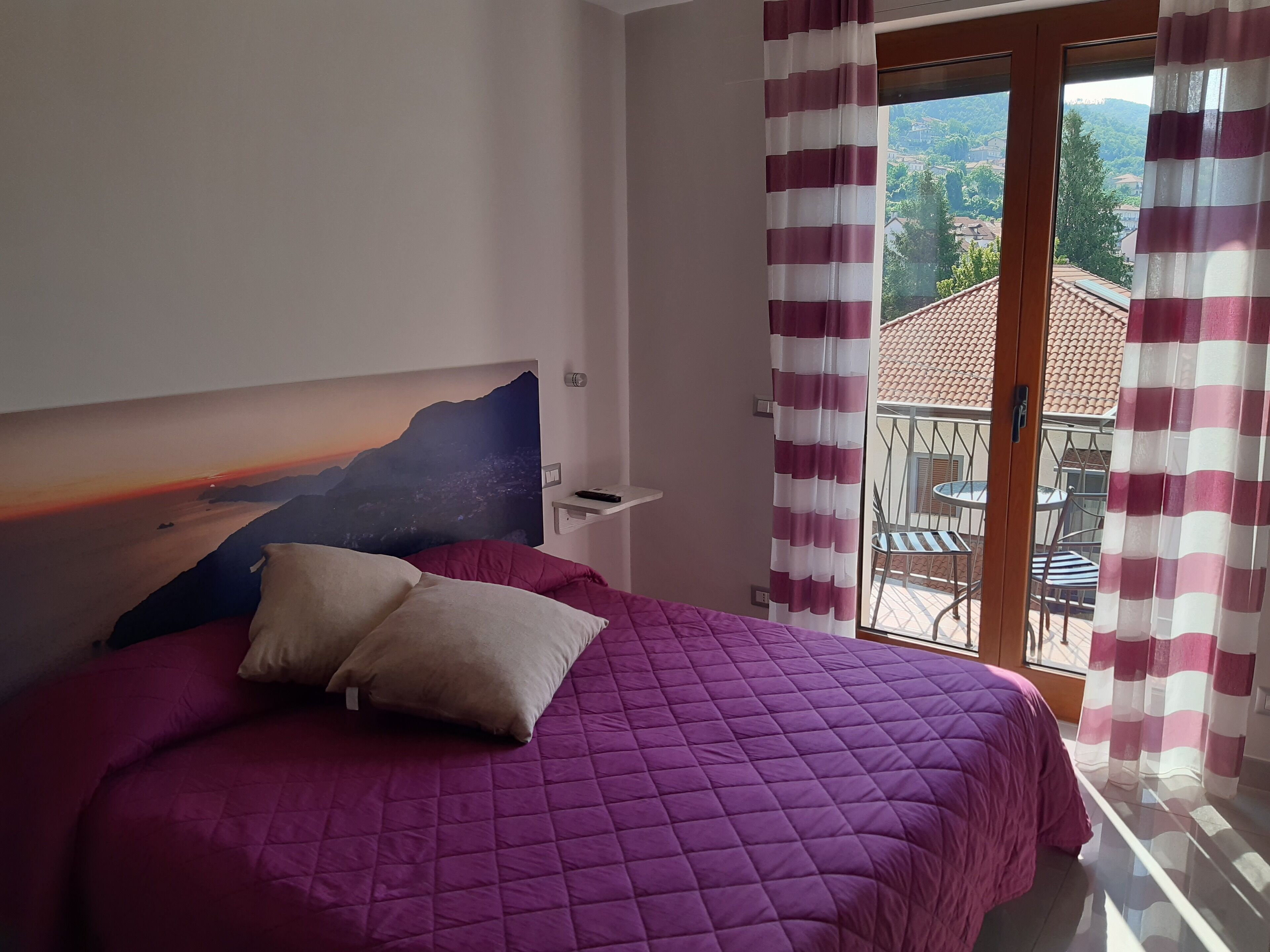 Un dormitorio con cama, mesita de noche y vistas a un balcón con sillas y una mesa.