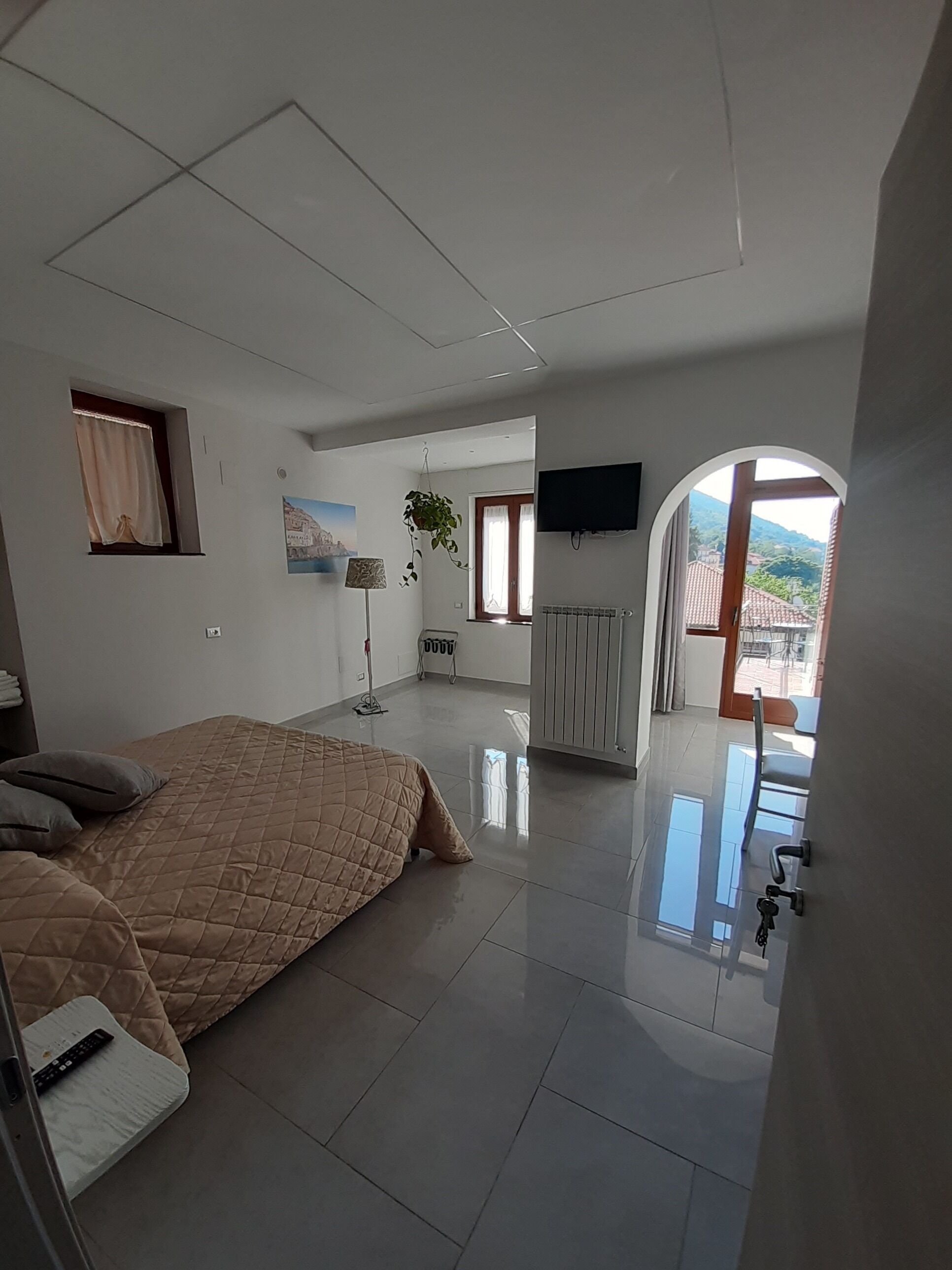 Un dormitorio moderno con una cama grande, un televisor de pantalla plana, una planta en maceta y vistas al exterior a través de una ventana.
