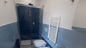 Uma casa de banho moderna com cabine de duche em vidro, duas sanitas, um bidé, uma pia e um porta-toalhas.