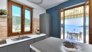 A modern kitchen with a large island, a built-in sink, and a view of the sea through an open door. - La Vela Deluxe lakefront in Salò (Salò)