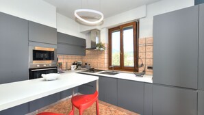 A modern kitchen with grey cabinets, a white countertop, a stainless steel oven, a microwave, and a red bar stool. - La Vela Deluxe lakefront in Salò (Salò)