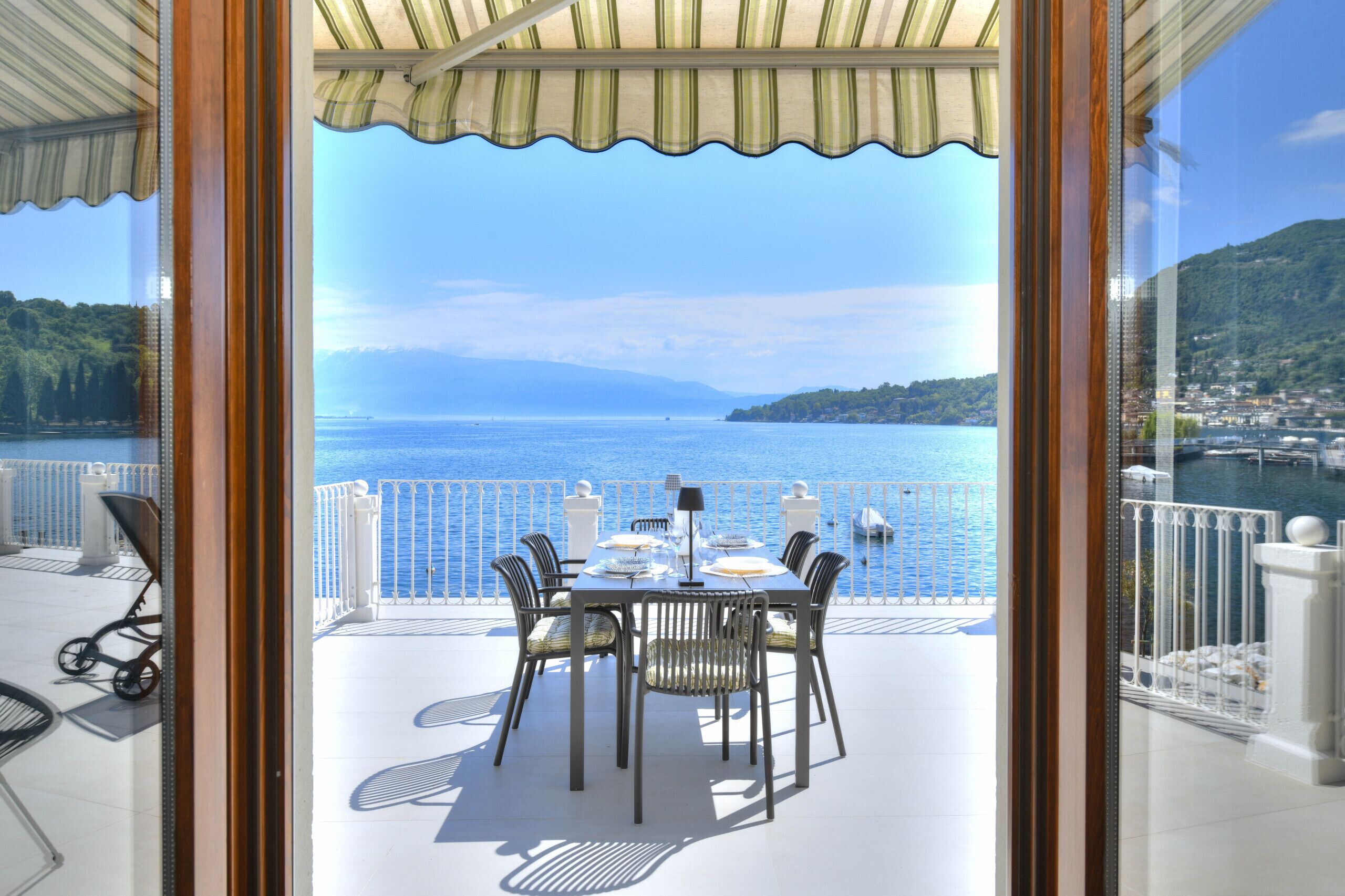 An outdoor dining area with a table and chairs, overlooking a body of water and a hilly landscape.