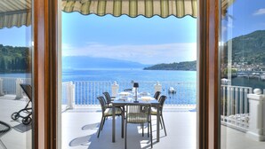 An outdoor dining area with a table and chairs, overlooking a body of water and a hilly landscape. - La Vela Deluxe lakefront in Salò (Salò)