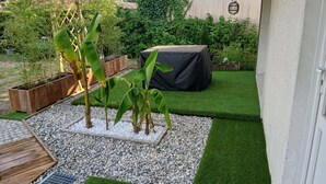 Un jardin avec une pelouse artificielle, un jardinier en bois et une table recouverte d’un tissu noir.