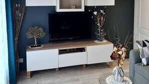 Un salon moderne avec un téléviseur à écran plat, un meuble de rangement blanc et une table basse en verre.