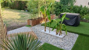 Un jardin avec une pelouse artificielle, un jardinier en bois et une table recouverte d’une nappe noire.
