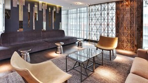 Un área de descanso moderna con un sofá, dos sillones, una mesa de centro de vidrio y una pared decorativa con elementos verticales.