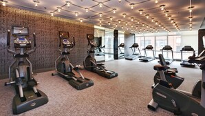 Un gimnasio con cintas de correr, elípticas y bicicletas estáticas, que presenta una pared con diseño e iluminación en el techo.