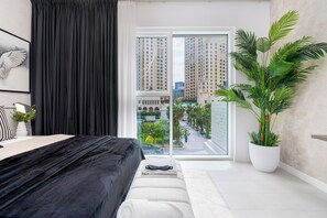 Een moderne slaapkamer met een groot bed, uitzicht op hoge gebouwen en een kamerplant.