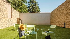 Une cour avec des murs en pierre, des chaises vertes, un chapeau et un sac.