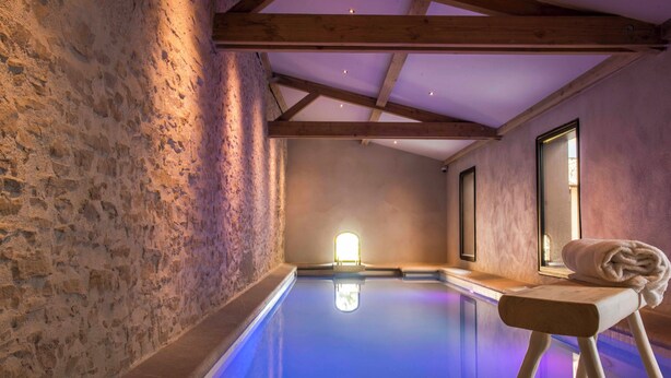 Une salle de spa avec un plafond en bois, des murs en pierre et une piscine illuminée de lumière bleue.