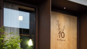 Une porte en bois ornée de motifs floraux et portant le numéro 10, une plante en pot et un lit avec une lampe en arrière-plan.