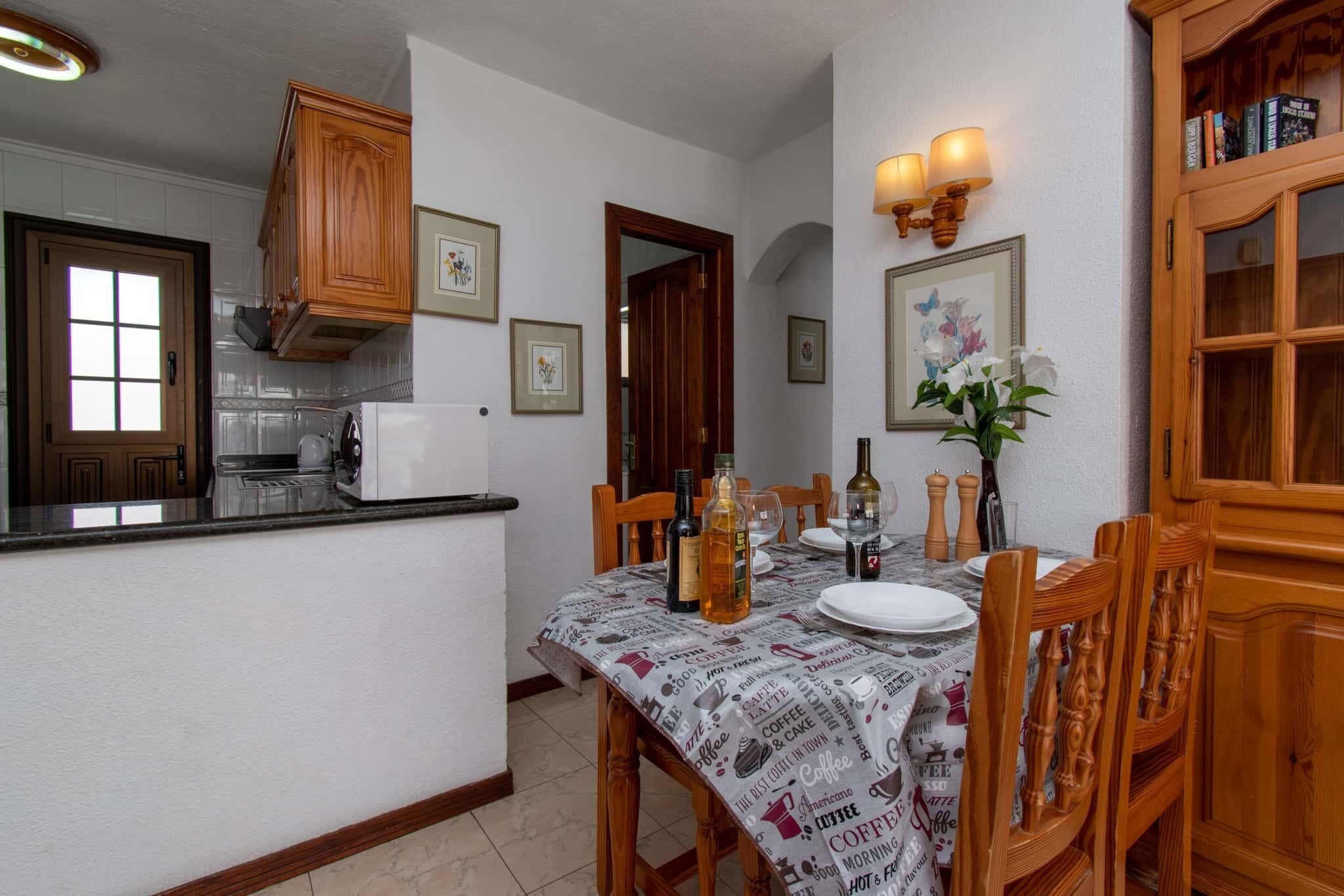 Un comedor con una mesa preparada para cuatro personas, sillas de madera, una mesita de centro e iluminación empotrada en la pared.
