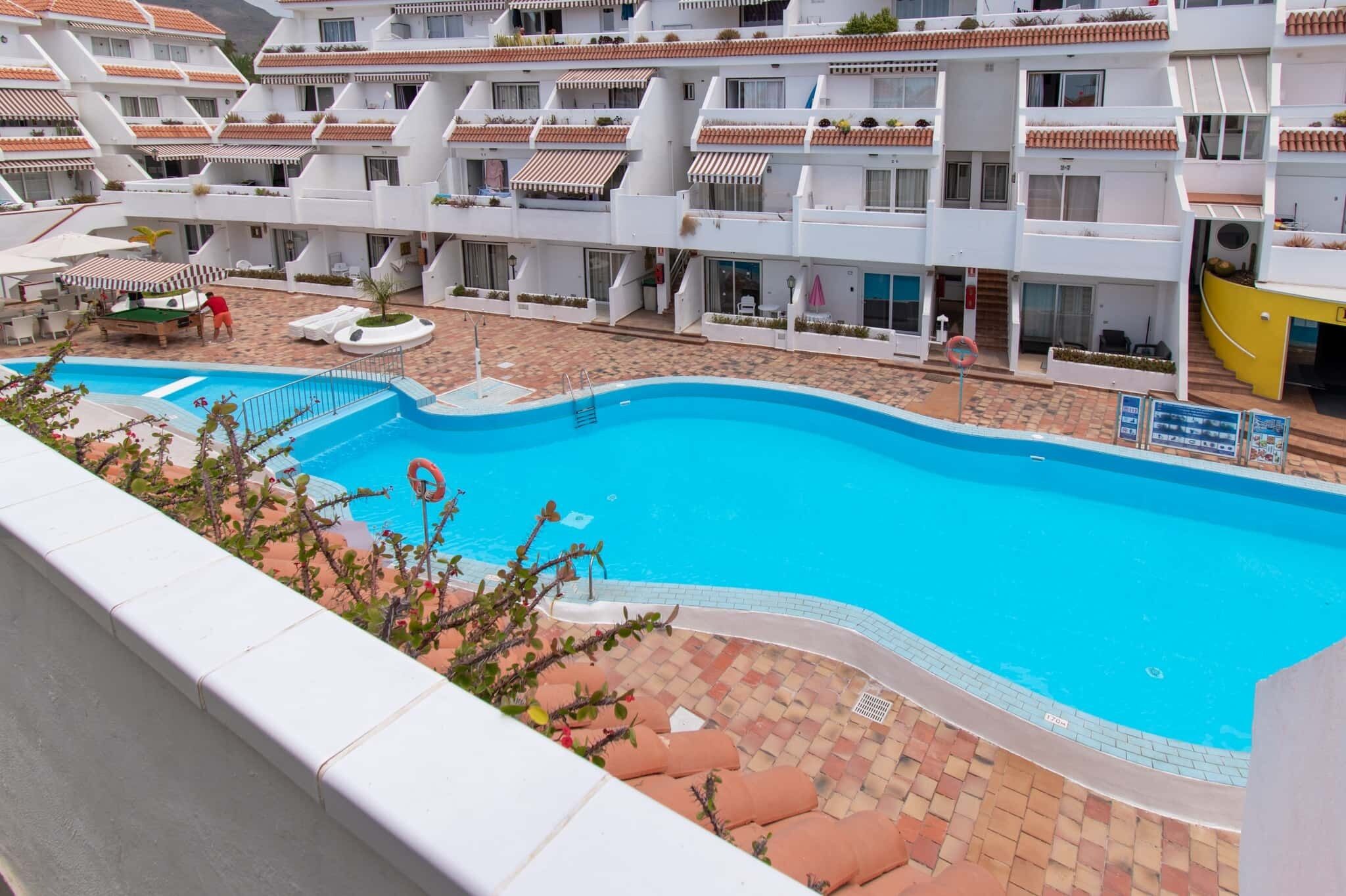 Un hôtel doté d’une piscine entourée d’une terrasse carrelée, de nombreux balcons et d’espaces de détente en plein air.