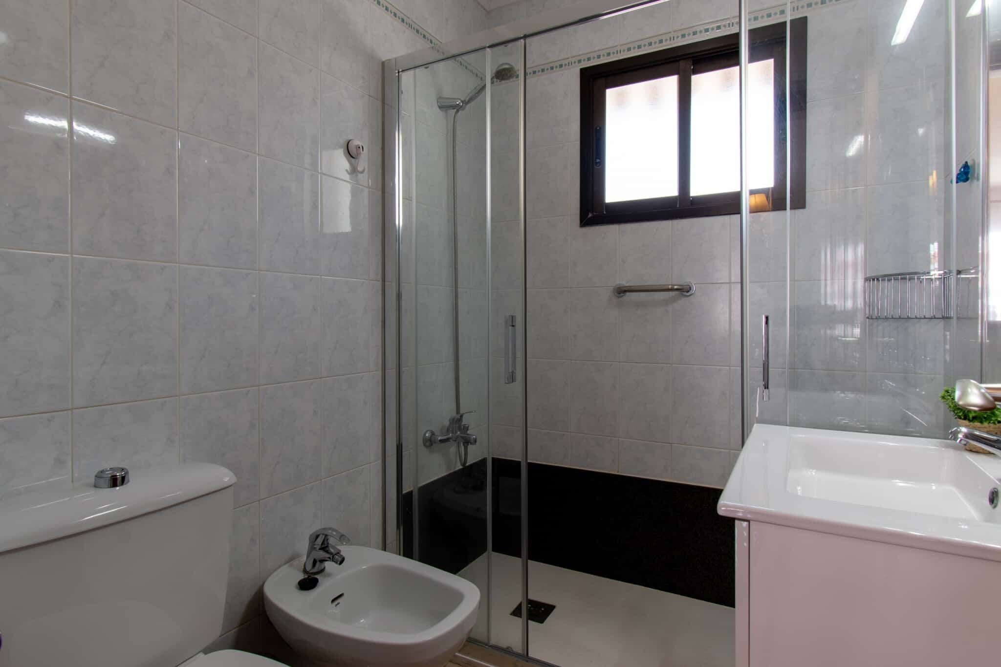 A modern bathroom with a glass-enclosed shower, a white sink, and a bidet.