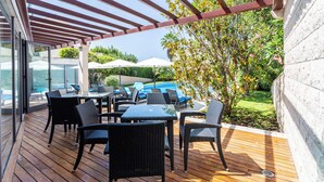 Une terrasse extérieure dotée d’un plancher en bois, de meubles en rotin noir et d’une pergola.